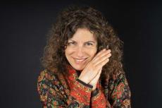 Femme souriante aux cheveux bouclés, portant une veste colorés à motifs rouges, verts et dorés