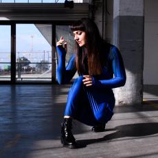 Une femme accroupie dans un espace industril. Elle porte une combinaison bleue à manches longues