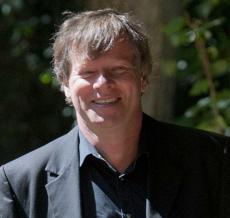 Un homme souriant avec cheveux courts portant un costume noir