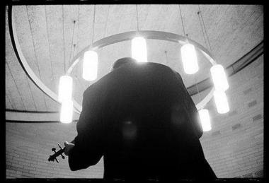 Photo noir et blanc d'un homme de dos qui joue de son instrument sous une lumière