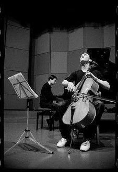 Photo noir et blanc d'un homme qui joue du violoncelle, et derrière lui un homme joue du piano