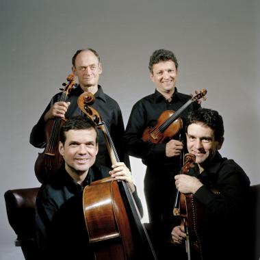Photo du Quatuor Sine Nomine : deux des membres sont assis, les deux autres sont debout derrière eux. Les quatre membres tiennent leurs instruments en main.