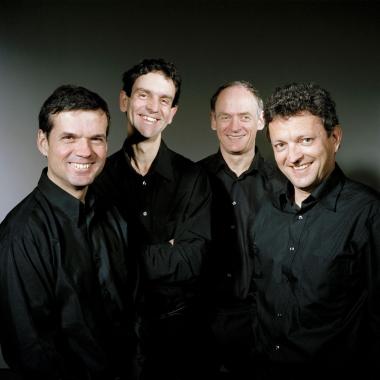 Photo du Quatuor Sine Nomine : les quatre hommes se tiennent debout avec des vêtements noirs et sourient à la caméra
